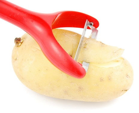 Peeling a potato with peeler on white